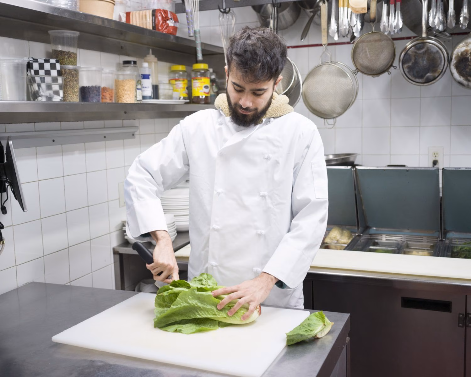 Chef White Coat Chops Romaine Lettuce Cutting Board Chef in white coat chops romaine lettuce on a cutting board in a commercial kitchen.