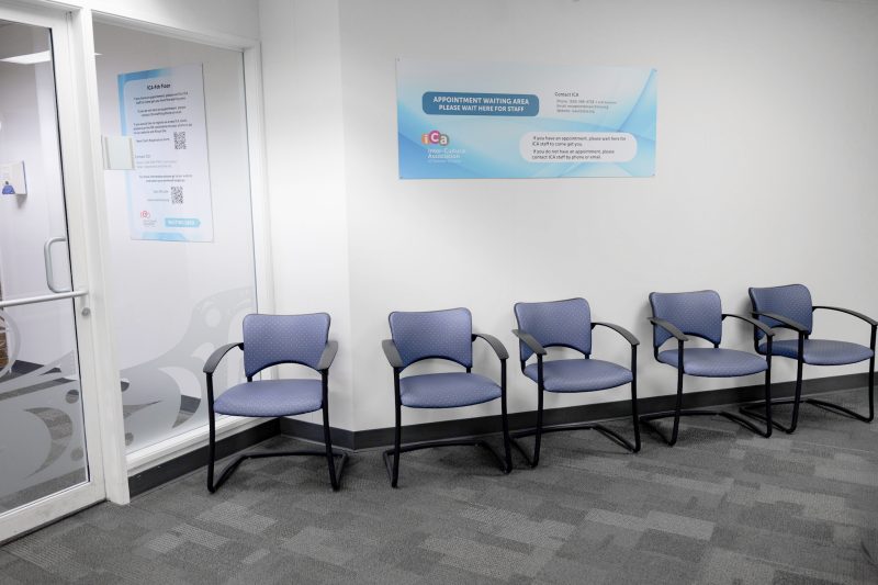 A waiting area with five blue chairs in front of a white wall with a sign.